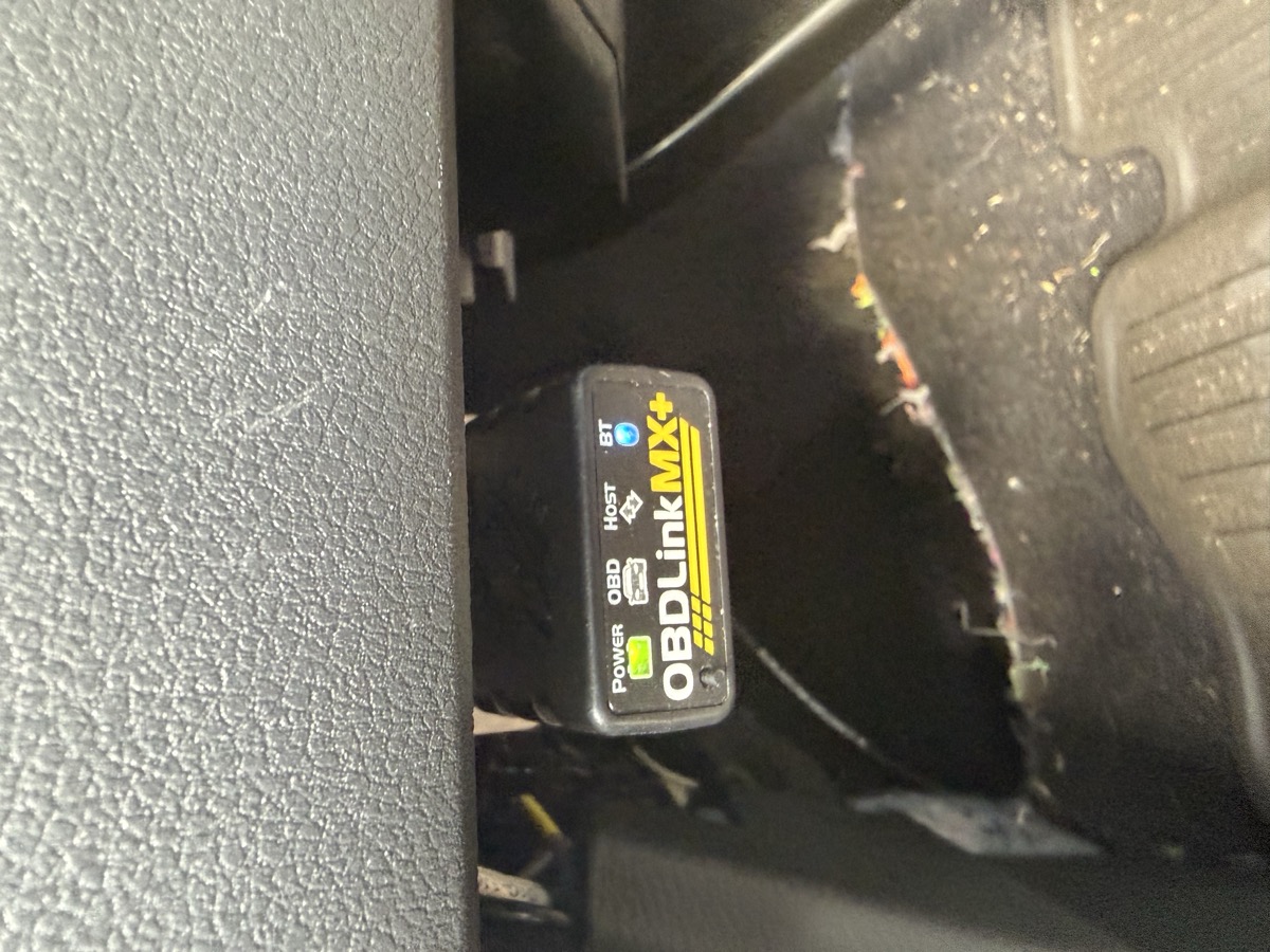 The OBD-II port under the dash with a Bluetooth adapter plugged in.
